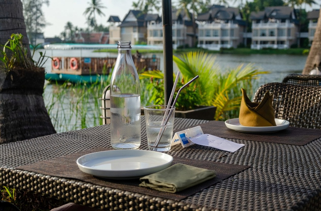 Reusable glass water bottle and metal and paper straws on a lakeside table (illustration) Reusable glass water bottle and metal and paper straws on a lakeside table (illustration)
